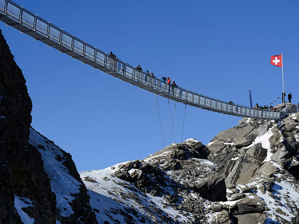 Хора ходят по висящ мост в ледника Les Diablerets, Швейцария. Алеята e с дължина 107 м и ширина 80 см и предлага зашеметяваща гледка към Алпите