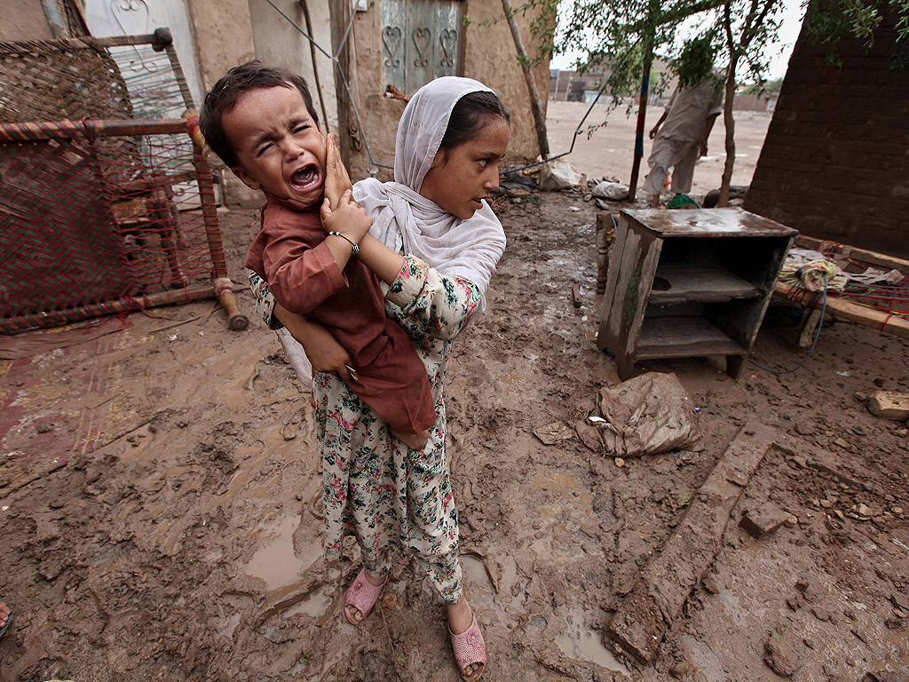Млада жена с малко дете оглежда руините на дома си след наводнение в Пешавар, Пакистан, на 16 август