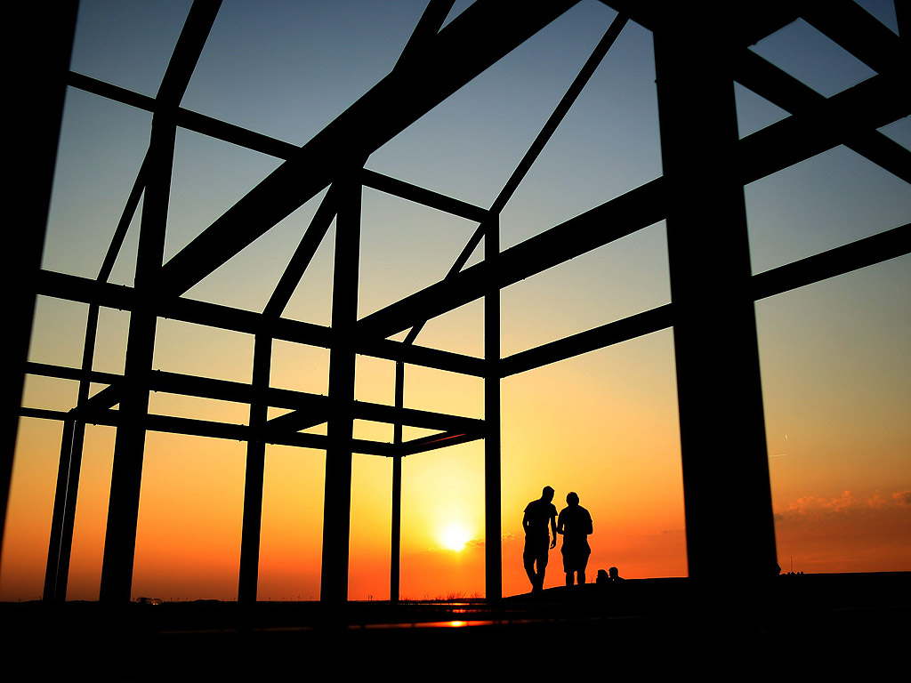 Двама души по залез слънце при изграждане на произведение на изкуството, под формата на къща, в Нойкирхен-Влин, Северна Германия