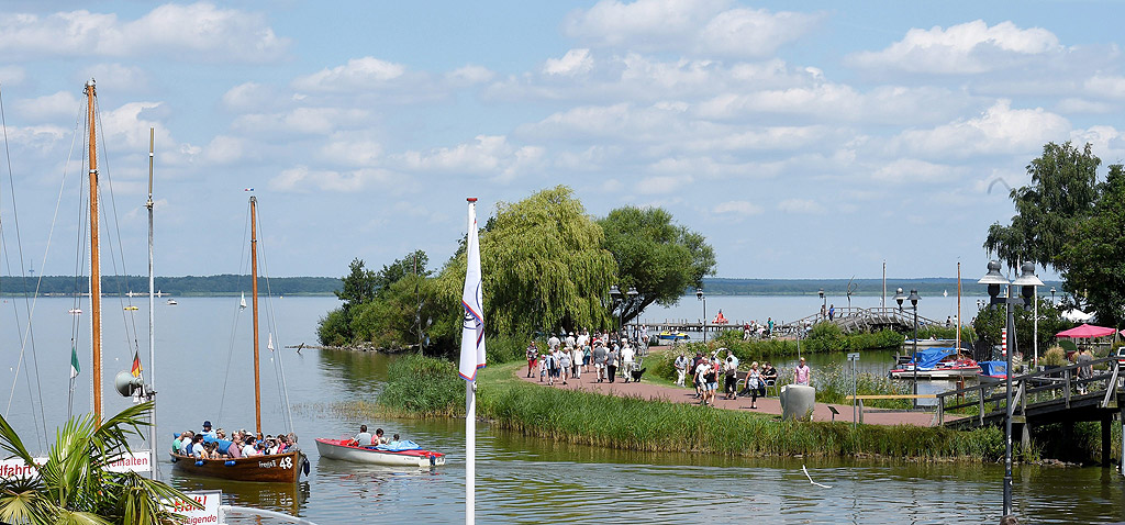 Лодки в топлото лятно време над езерото Steinhude в региона на Хановер, Германия, докато хората ходят по крайбрежна алея