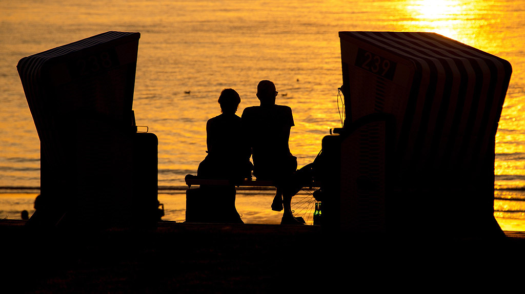 Хора, седнали на пейка между два шезлонга на плажа в Нордерней, Германия